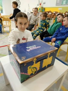 Dzieci w przedszkolu siedzą przy stole z kufrem lakomozucha