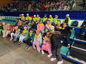 Grupa dzieci siedzi na trybunach stadionu, w tle widoczna publiczność