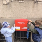 Dwoje dzieci wkłada listy do czerwonej skrzynki pocztowej
