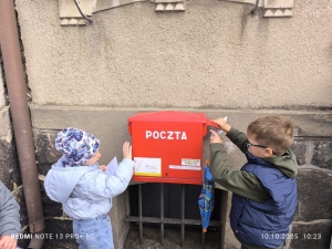 Dwoje dzieci wkłada listy do czerwonej skrzynki pocztowej