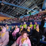 Grupa dzieci i dorosłych na trybunach w hali sportowej