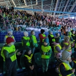 Grupa dzieci w żółtych kamizelkach na trybunach stadionu