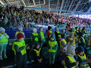 Grupa dzieci w żółtych kamizelkach na trybunach stadionu