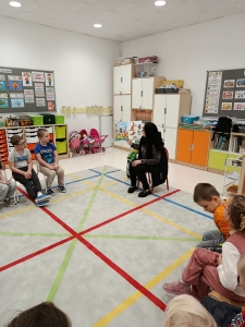 Grupa dzieci siedzi na podłodze w klasie, słuchając kobiety