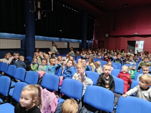 Grupa dzieci siedzi na niebieskich fotelach w dużej sali