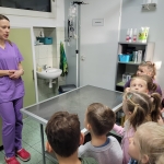 Kobieta w fioletowym stroju medycznym mówi do grupy dzieci