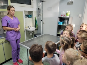 Kobieta w fioletowym stroju medycznym mówi do grupy dzieci