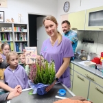 Kobieta w fioletowym stroju lekarskim trzyma bukiet kwiatów. (Długość: 54 znaków)