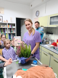 Kobieta w fioletowym stroju lekarskim trzyma bukiet kwiatów. (Długość: 54 znaków)