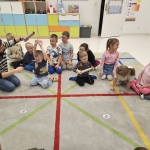 Grupa dzieci siedzi na podłodze wokół kobiety, która coś pokazuje