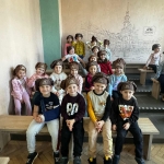 Grupa dzieci w czapkach siedzi na ławkach w pomieszczeniu