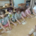 Dzieci w czapkach kuchennych robią ciasto na stole