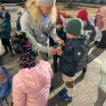 Kobieta w czapce daje dziecku w zimowej czapce coś do ręki. (49 znaków)