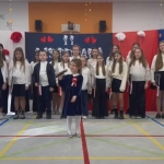 Grupa dzieci w strojach szkolnych stoi na sali gimnastycznej