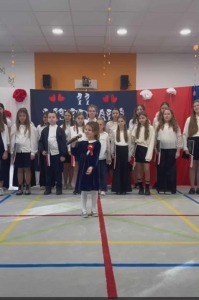 Grupa dzieci w strojach szkolnych stoi na sali gimnastycznej