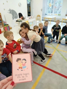 Dzieci siedzą w klasie, jedna dziewczynka obejmuje koleżankę