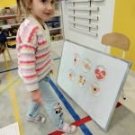 Dziewczynka stoi obok tablicy z obrazkami w przedszkolu
