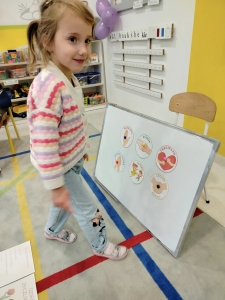 Dziewczynka stoi obok tablicy z obrazkami w przedszkolu