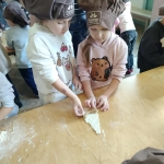 Dwie dziewczynki w czapkach kuchennych lepią ciasto na stole