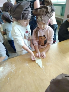 Dwie dziewczynki w czapkach kuchennych lepią ciasto na stole