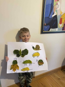 Chłopiec trzyma rysunek z liśćmi w kształcie zwierząt