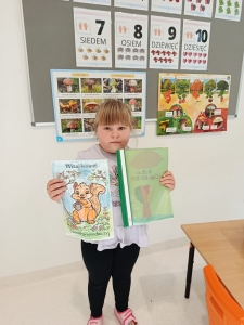 Dziewczynka trzyma dwie książki w klasie przed tablicą