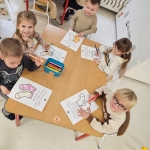 Dzieci siedzą przy stole i kolorują obrazki