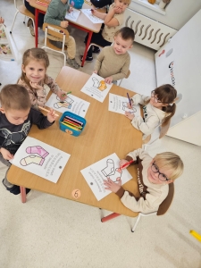 Dzieci siedzą przy stole i kolorują obrazki