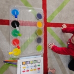 Dzieci siedzą na podłodze z zestawem do mieszania kolorów. (49 znaków)