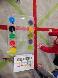 Dzieci siedzą na podłodze z zestawem do mieszania kolorów. (49 znaków)