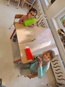 Dwie dziewczynki siedzą przy stole z dużymi ołówkami