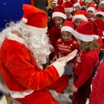 Mikołaj czyta książkę grupie dzieci w czerwonych czapkach