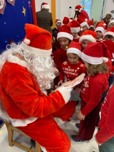Mikołaj czyta książkę grupie dzieci w czerwonych czapkach