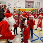 Dzieci w czerwonych czapkach i ubraniach spotykają się z Mikołajem w szkole