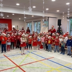 Grupa dzieci w czerwonych ubraniach i czapkach Mikołaja podczas występu