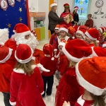 Dzieci w strojach Mikołaja otaczają Świętego Mikołaja w szkole