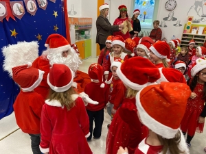 Dzieci w strojach Mikołaja otaczają Świętego Mikołaja w szkole