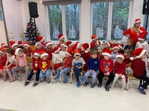 Grupa dzieci w czapkach Mikołaja siedzi na krzesłach w sali