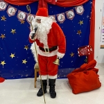 Mikołaj w czerwonym stroju stoi przed festiwalną dekoracją