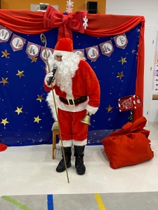 Mikołaj w czerwonym stroju stoi przed festiwalną dekoracją