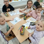 Dzieci siedzą przy stole i kolorują rysunki