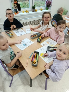 Dzieci siedzą przy stole i kolorują rysunki