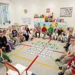 Grupa dzieci i nauczycielki w przedszkolu, siedzące na podłodze