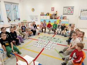 Grupa dzieci i nauczycielki w przedszkolu, siedzące na podłodze