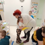 Kobieta w peruce i białym płaszczu całuje dziewczynkę w klasie