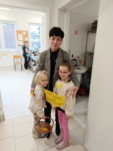 Kobieta z dwiema dziewczynkami trzymającymi żółty plakat. (44 znaki)