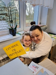 Kobieta i dziewczynka trzymają żółty plakat z napisem "Czy mogę cię przytulić?"