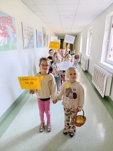 Dzieci w szkolnym korytarzu trzymają plakaty z napisami