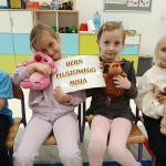 Dwie dziewczynki trzymają tabliczkę z napisem "Dzień Pluszowego Misia"