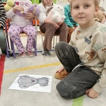 Dzieci siedzą w szkolnej sali, jedno dziecko na podłodze